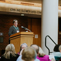 Ann Smith, standing at a podium, addressing the audience sitting at tables