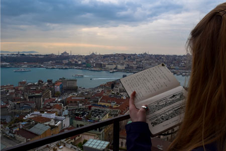 person holding a book on a balcony looking over a city