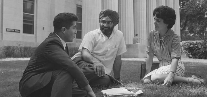 Three students sit on the lawn in front of the columns of Burton Hall