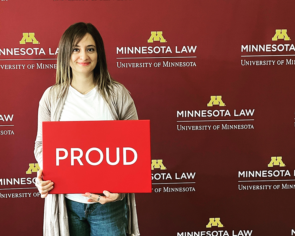 Shaghek Manjikian holding a "proud" sign in front of a Minnesota Law background
