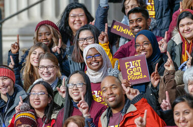 First-generation students pose with "first gen proud" signs on the steps outside Northrop Auditorium