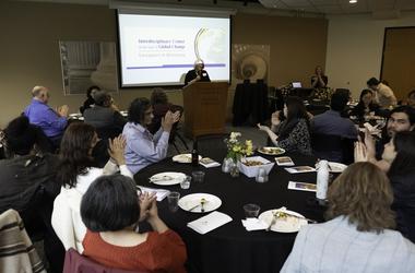 Attendees clap as Director Karen Brown speaks behind a lectern