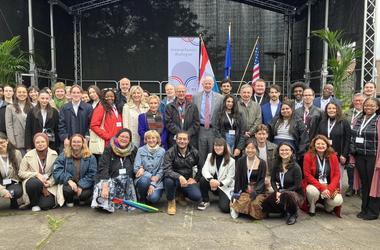 attendees of the Transatlantic Dialogue pose as a group in front of EU, U.S., and Luxembourg flags