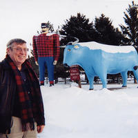 William Toscano in front of a statue of Paul Bunyan and Babe the blue ox in wintertime