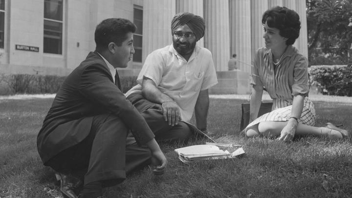 Three students sit on the lawn in front of the columns of Burton Hall