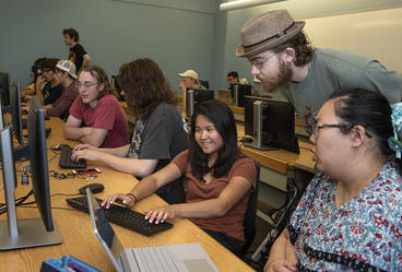 Teacher bending down to help students at computers